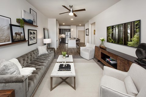 A living room with a grey couch, a white coffee table, and a painting of a forest on the wall.