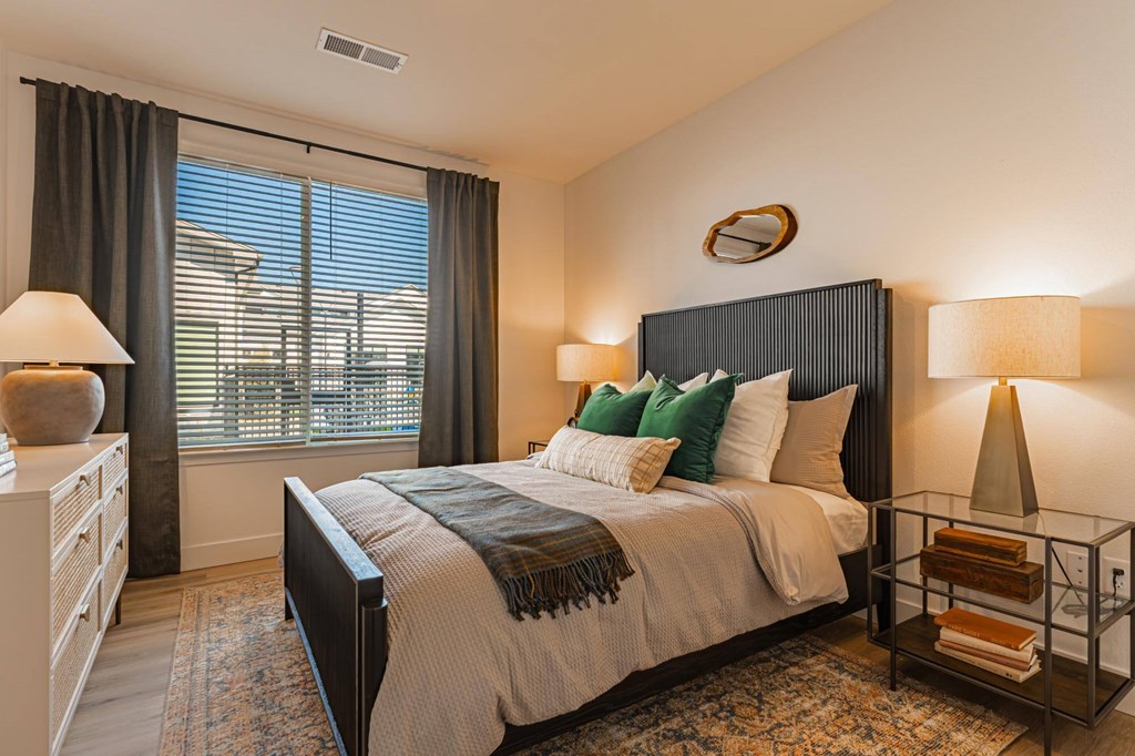 A bedroom with a large bed and a window with blinds.