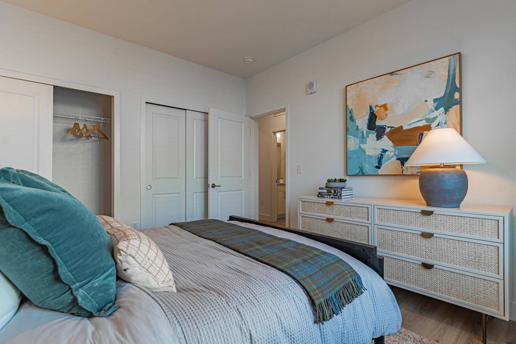 A bedroom with a bed, nightstand, and a painting on the wall.