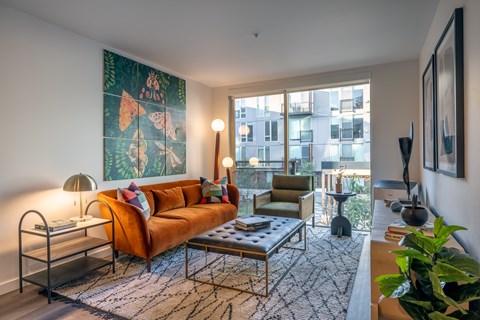 A living room with a large orange sofa and a painting on the wall.