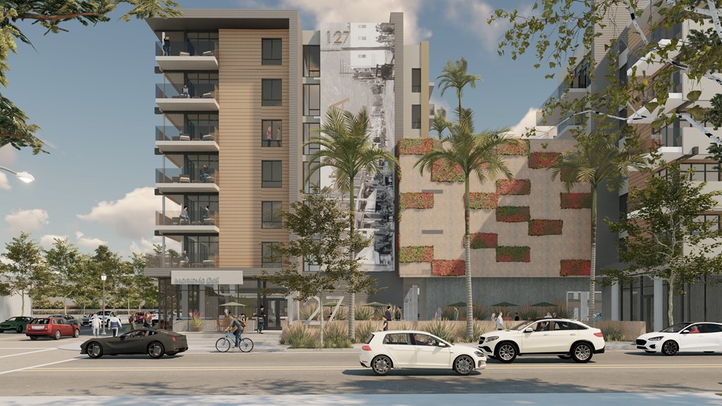 A street view of a modern building with cars parked in front and people walking on the sidewalk.