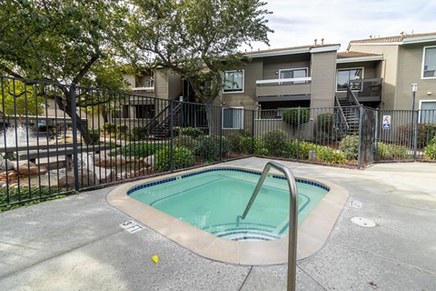 A small pool in a fenced in area in front of apartment buildings.