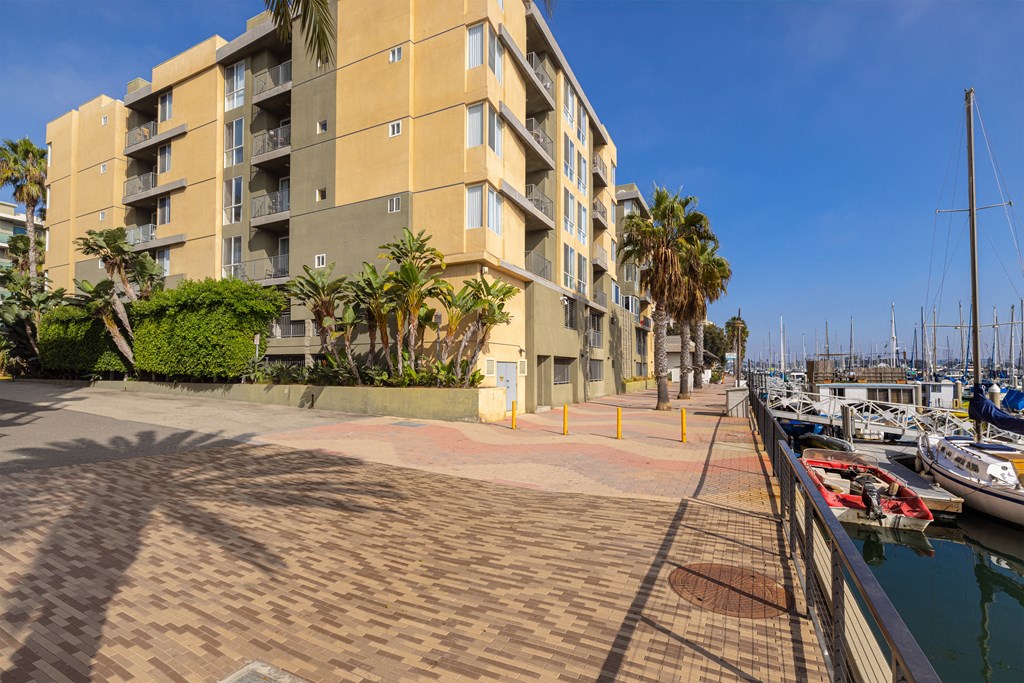 A marina with boats docked and a building with balconies in the background.