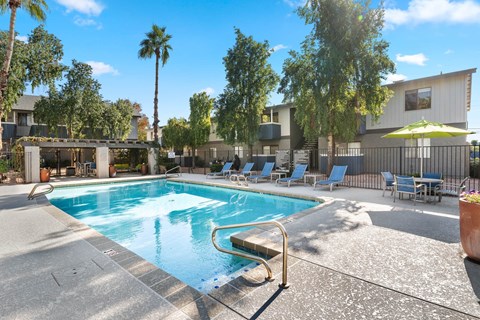 A pool surrounded by chairs and trees.