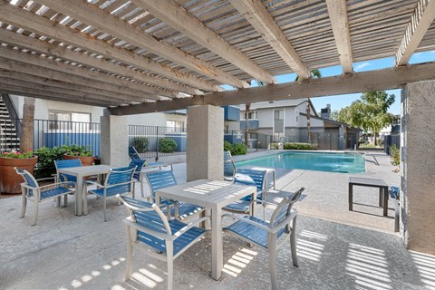 A patio with a table and chairs under a wooden pergola.