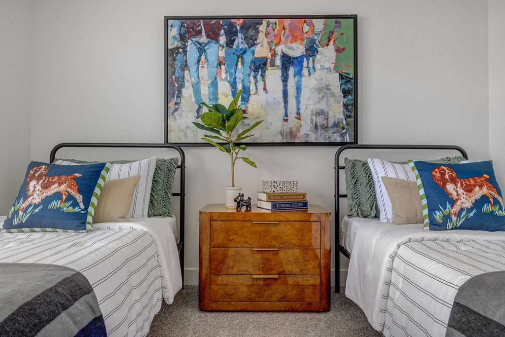 A bedroom with two beds, a nightstand, and a painting on the wall.