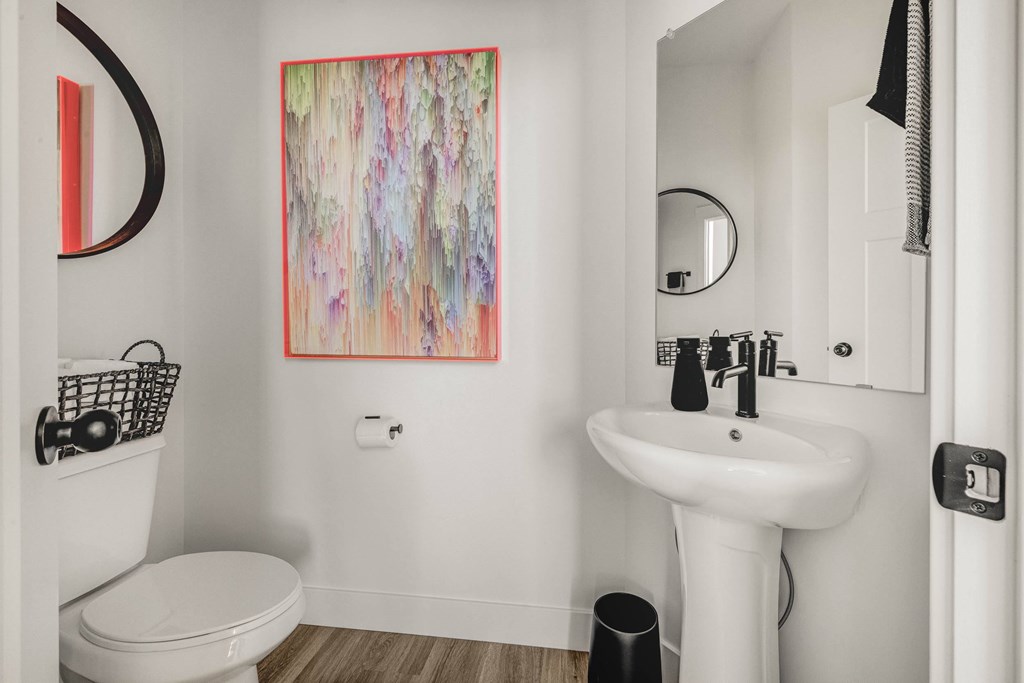 A bathroom with a white toilet, a white sink, and a colorful painting on the wall.