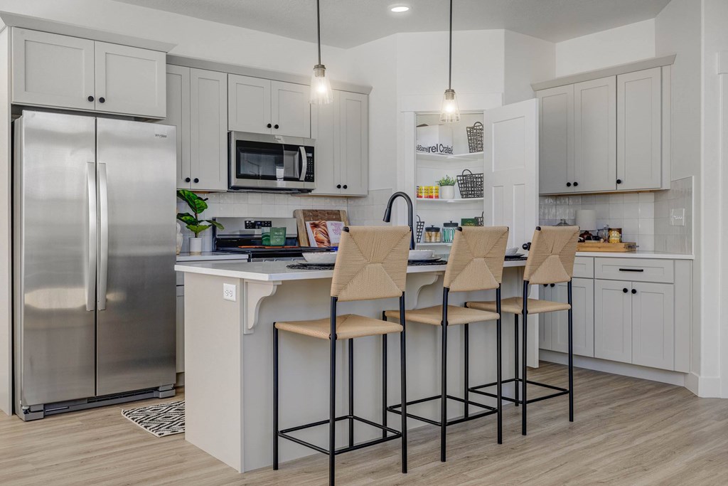 A kitchen with a refrigerator, microwave, and bar stools.