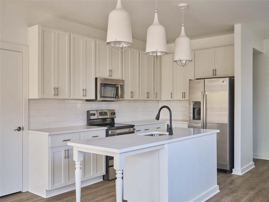 a white kitchen with a white island and stainless steel appliances