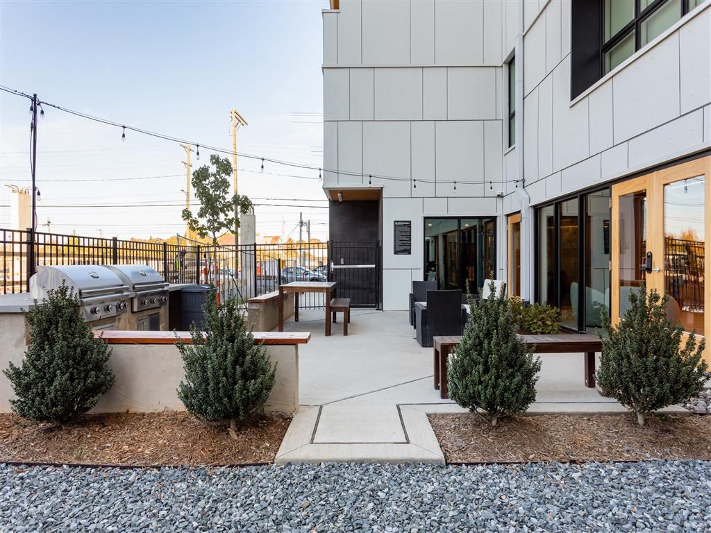 a patio with a grill and bushes in front of a building