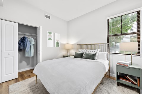 A bedroom with a large bed and a window with blinds.