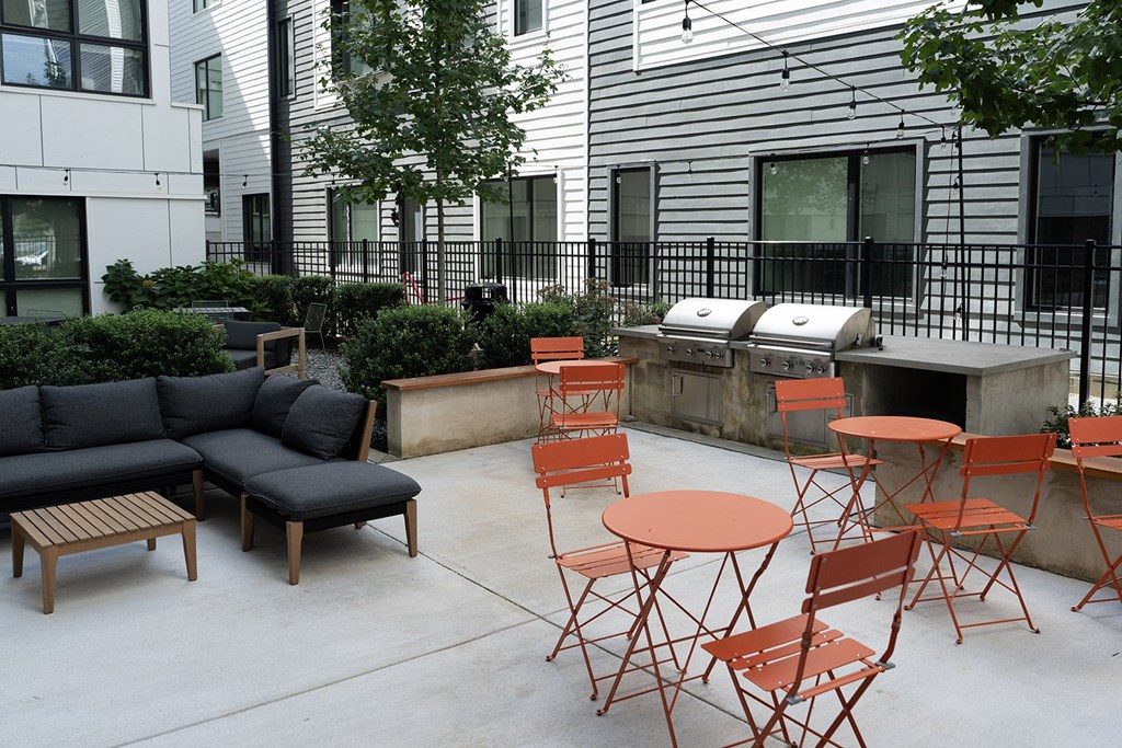 A patio with a black couch, orange chairs, and a grill.