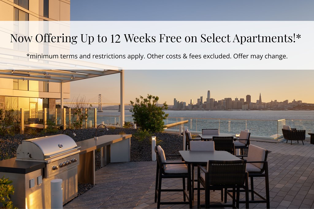 A modern outdoor kitchen area with a barbecue grill and seating area overlooking a city skyline at dusk.