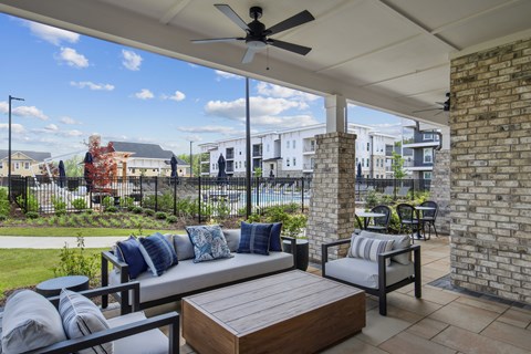 A patio with a couch, chairs, and a table with a fan overhead.