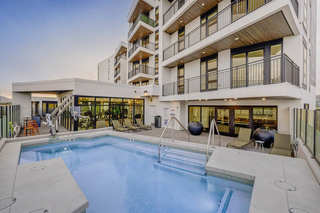 A large swimming pool is surrounded by a patio area with chairs and a hot tub.