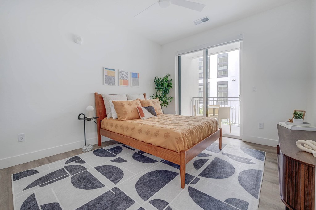 A bedroom with a bed, a rug, and a plant.