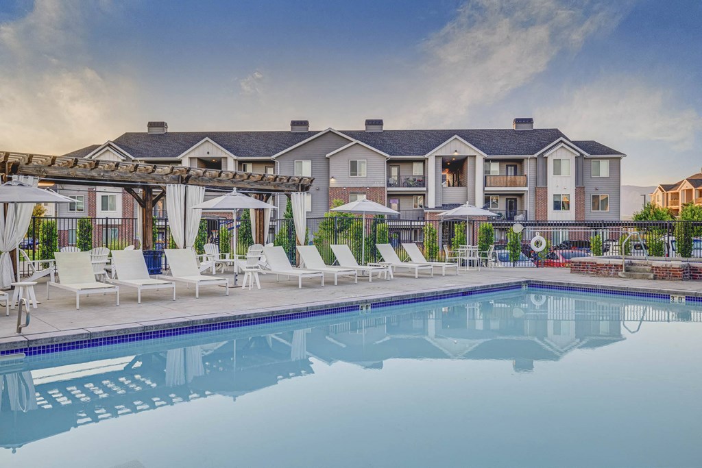 a swimming pool with chairs and umbrellas and a building in the background