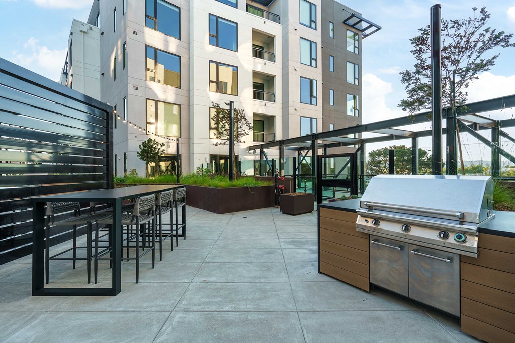 a patio with a grill and a table with chairs in front of an apartment building