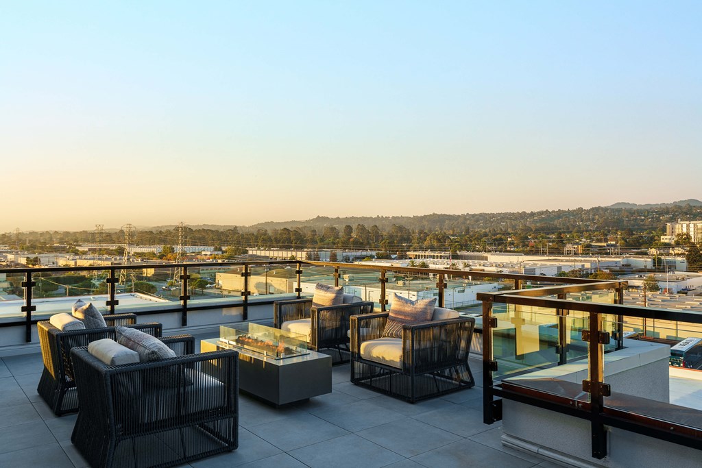 a rooftop terrace with tables and chairs overlooking a city at sunset
