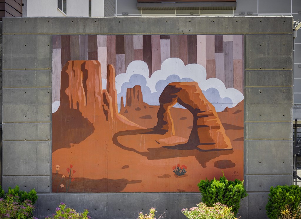 A mural of a desert scene with a large rock formation and a small plant in the foreground.