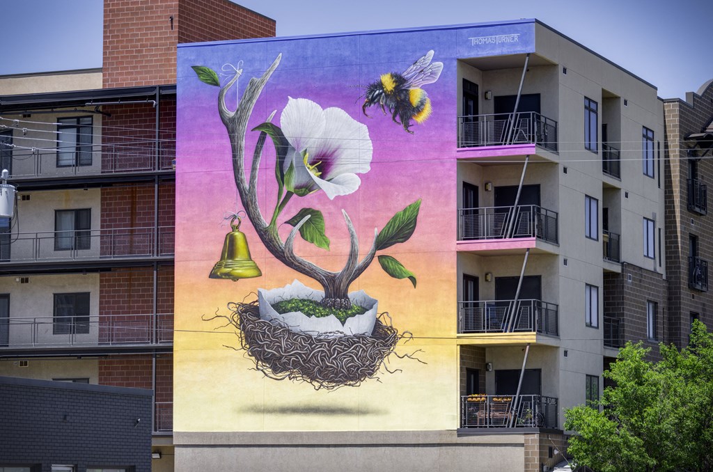 A mural of a flower with a bee and a bell on a building.
