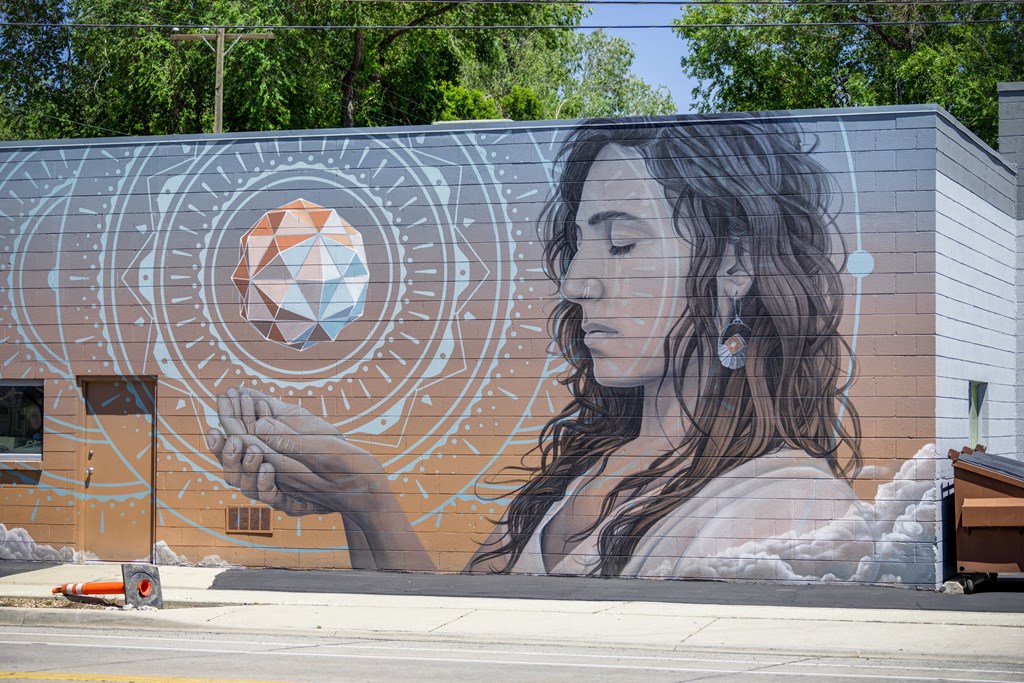 A mural of a woman holding a geometric object is painted on a building.