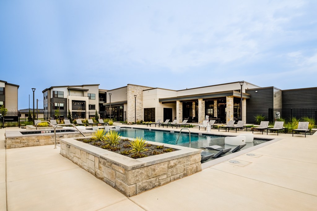 A pool surrounded by a concrete patio and a stone planter.