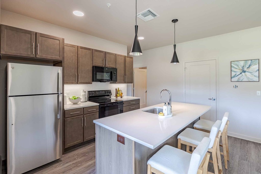A kitchen with a refrigerator, microwave, oven, sink, and cabinets.