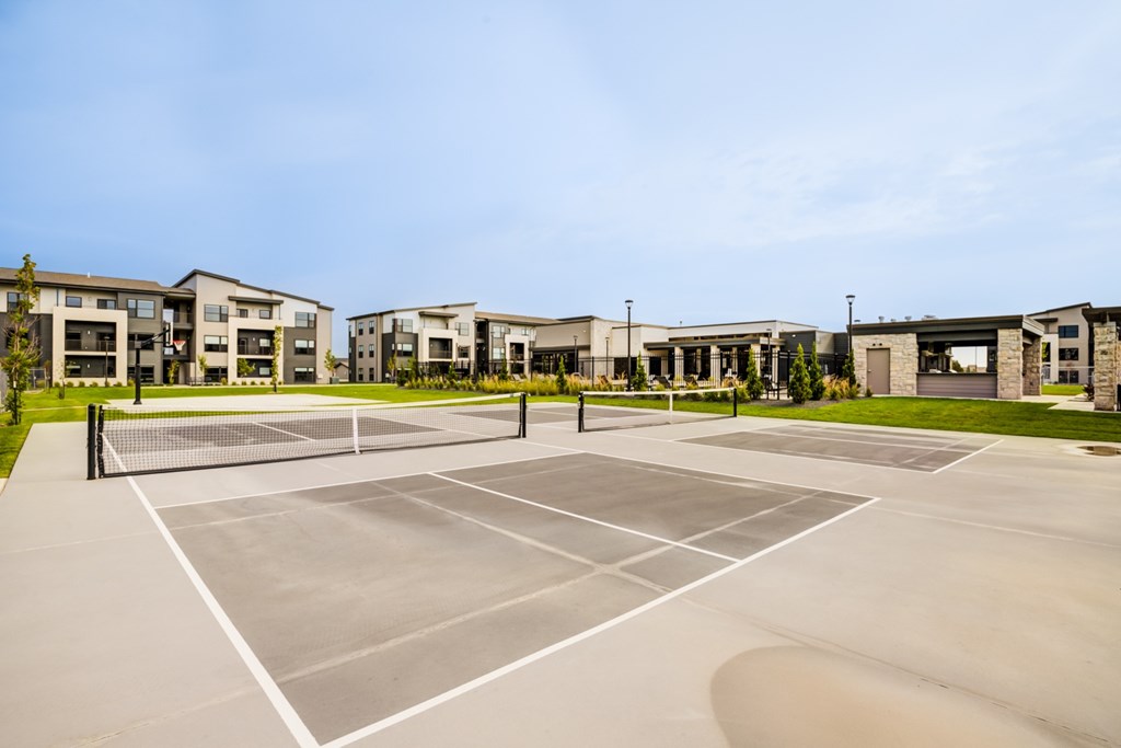 A tennis court is surrounded by apartment buildings.