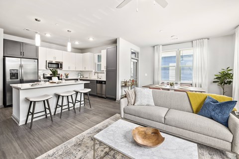 A modern kitchen with a bar area and a living room with a grey couch.
