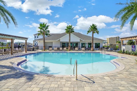 A large outdoor swimming pool surrounded by palm trees and a building in the background.