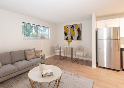 A modern living room with a grey sofa, a white coffee table, and a dining table set up with chairs.