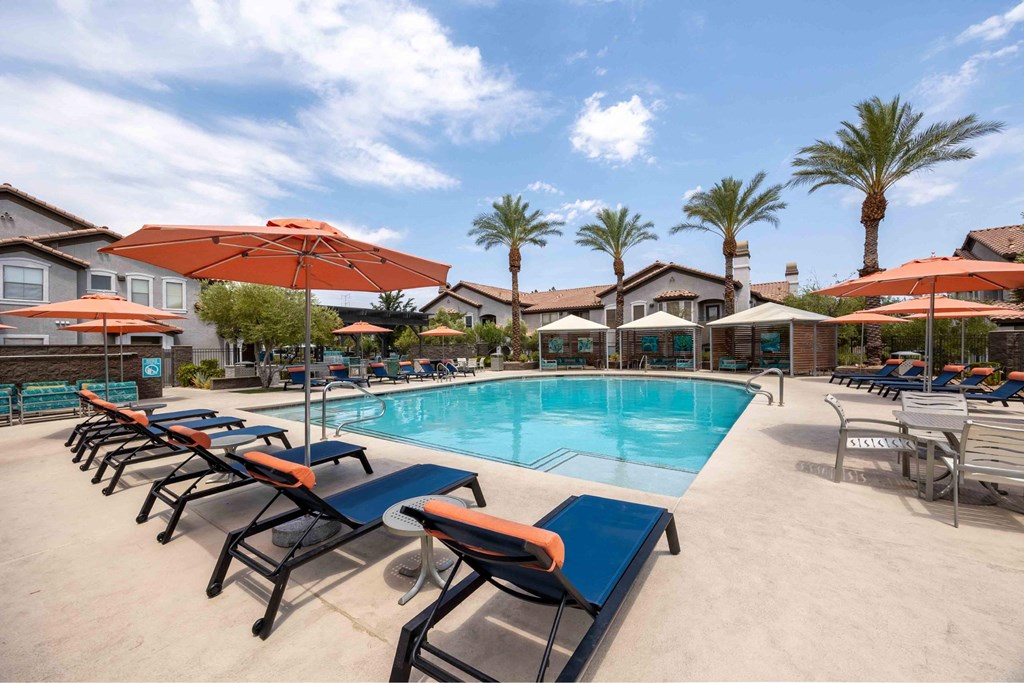 A pool with sun loungers and umbrellas is surrounded by palm trees.