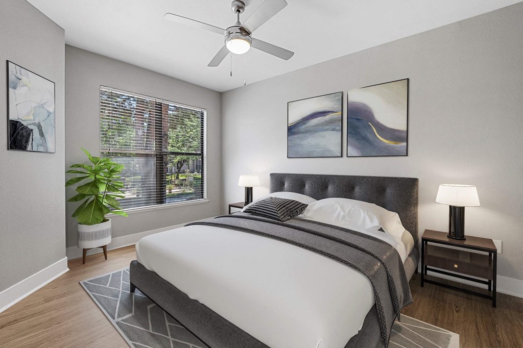 A bedroom with a large bed, a ceiling fan, and a potted plant.