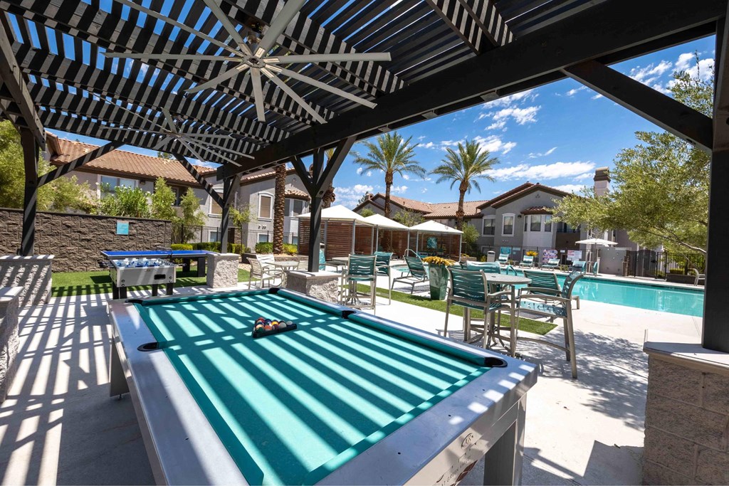 A pool table under a shaded area with a pool table in the foreground.