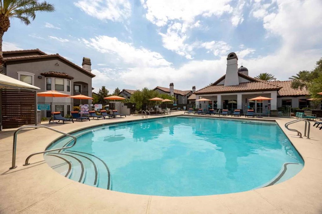 A large swimming pool in front of a building with a patio and umbrellas.