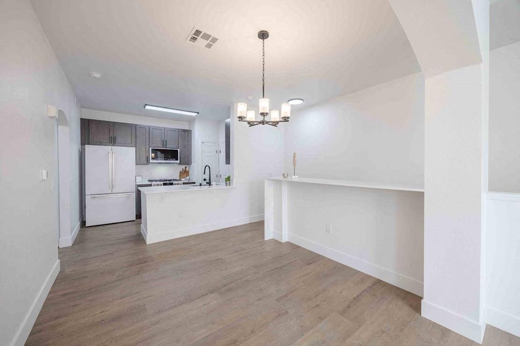 A kitchen with a white fridge and a white island with a chandelier hanging from the ceiling.
