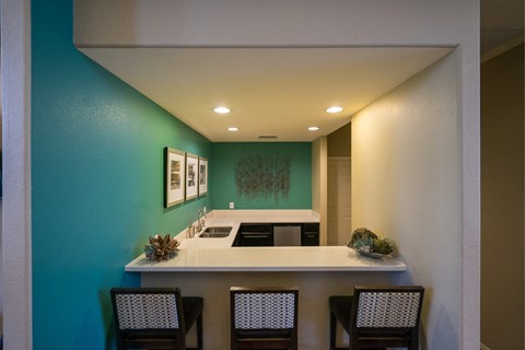 A kitchen with a white counter top and three chairs.