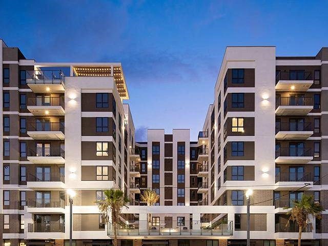 A modern apartment building with balconies and palm trees in front.
