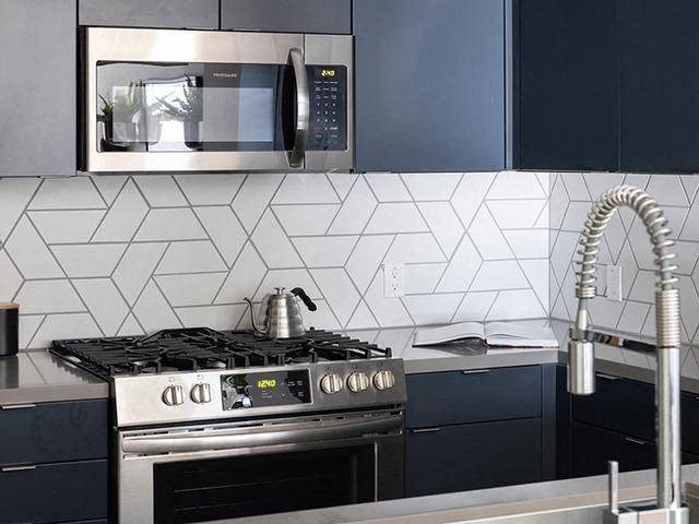 A modern kitchen with a stove, microwave, and a tile backsplash.