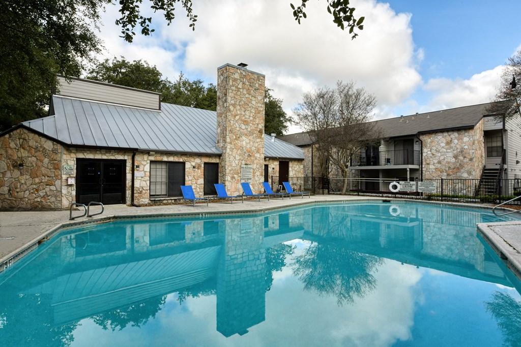 A swimming pool in front of a house with a stone chimney.