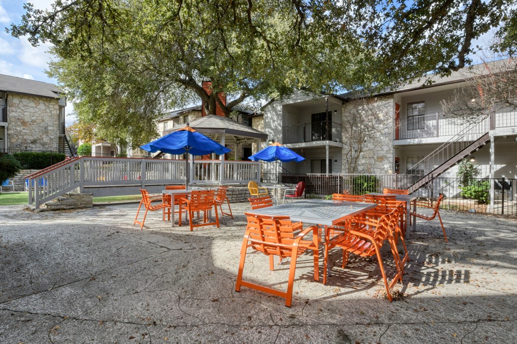 A patio with orange chairs and tables is surrounded by a fence and a building.