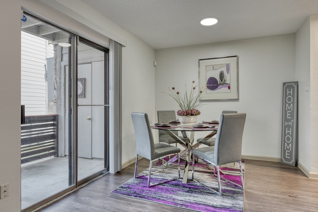 A dining room with a glass table and grey chairs.