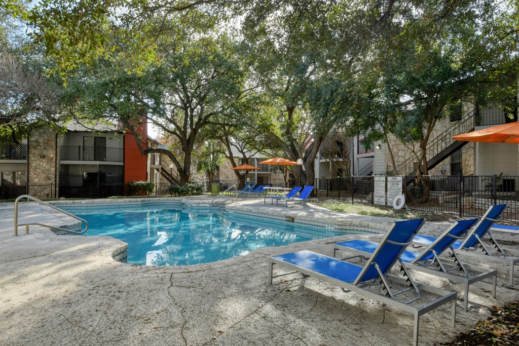 A pool surrounded by trees and chairs.
