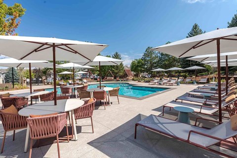 A poolside area with tables and chairs and umbrellas.