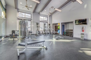 Large fitness center with concrete flooring and ceiling fans. Weight benches, yoga balls, and cardio machines - Photo Gallery 16