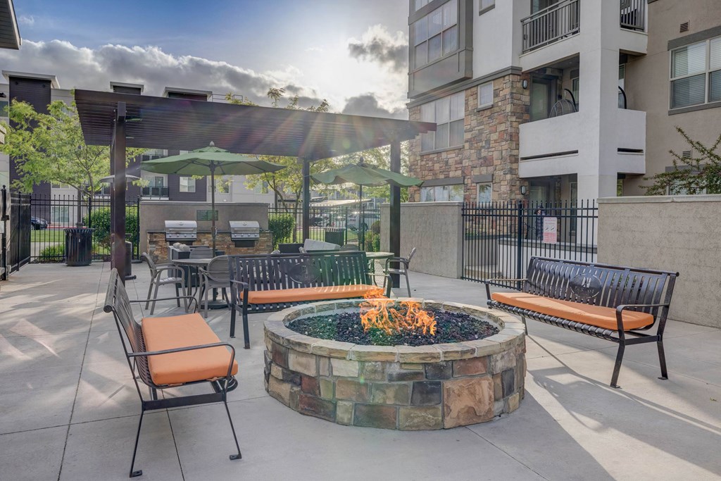 A sunny day at a courtyard with a fire pit, chairs, and a table.