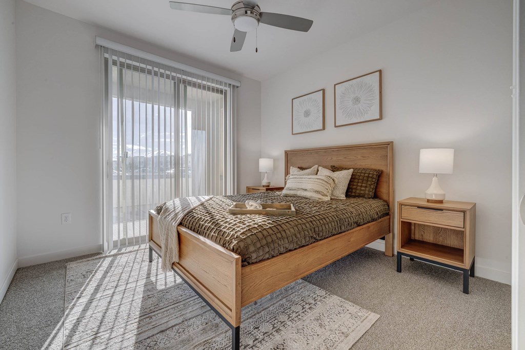 A bedroom with a bed, nightstand, and window with blinds.