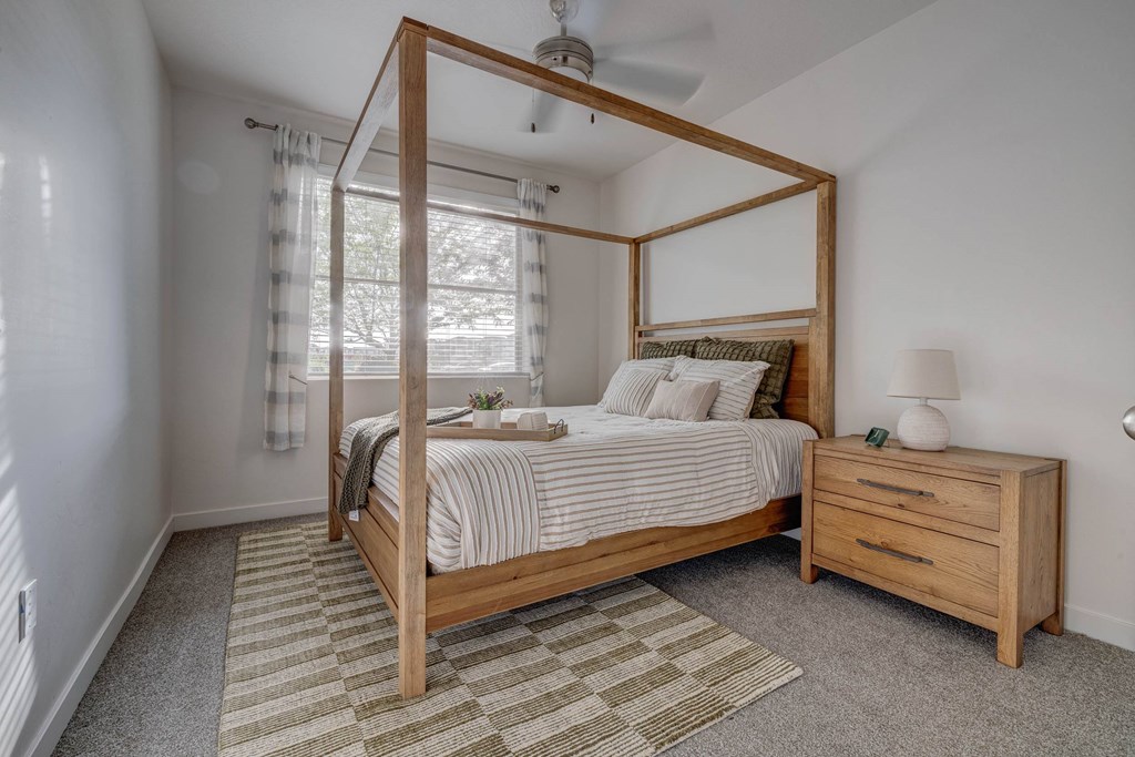 A bedroom with a four-poster bed, striped bedspread, and a small nightstand with a lamp.