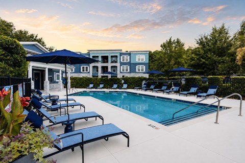 A pool surrounded by lounge chairs and umbrellas with a building in the background.